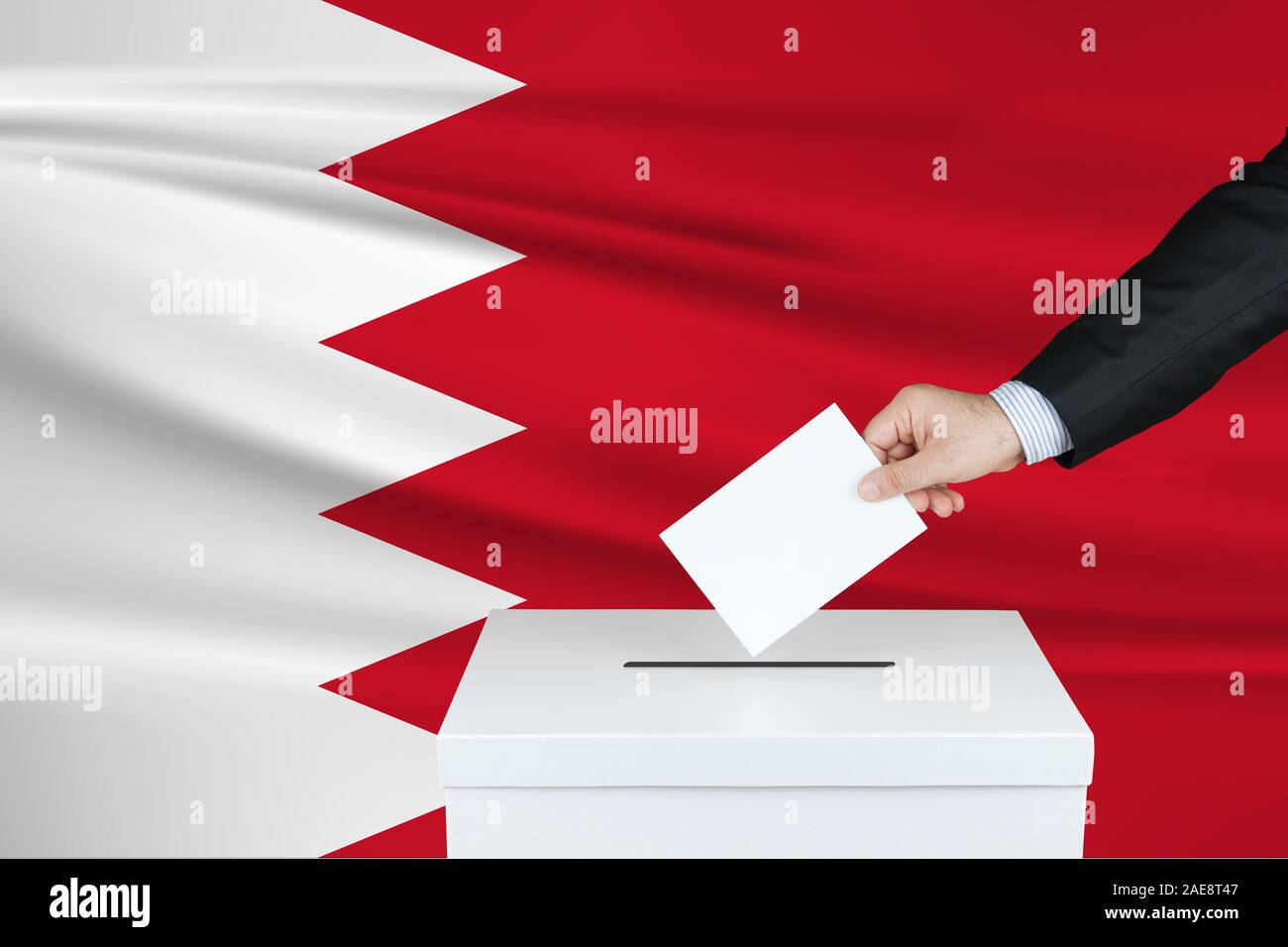Election in Bahrain. The hand of man putting his vote in the ballot box. Waved Bahrain flag on background. Stock Photo