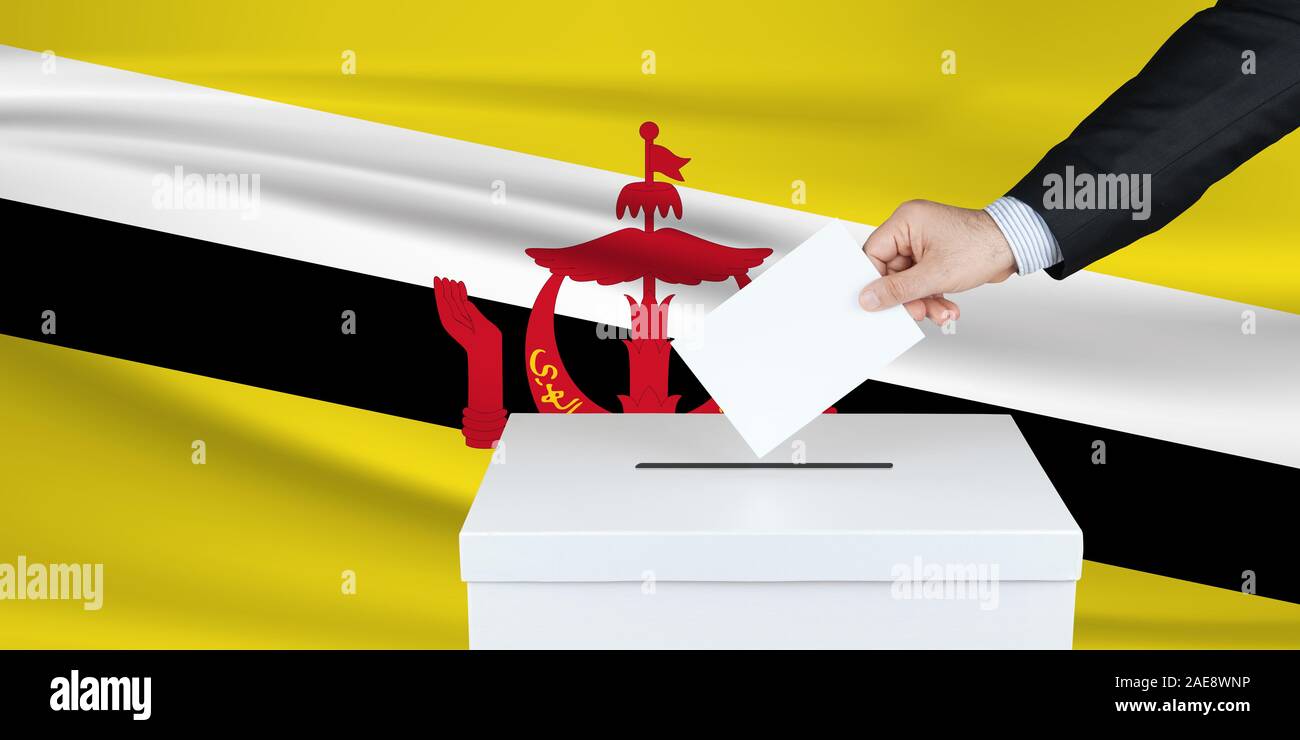 Election in Brunei. The hand of man putting his vote in the ballot box. Waved Brunei flag on background. Stock Photo