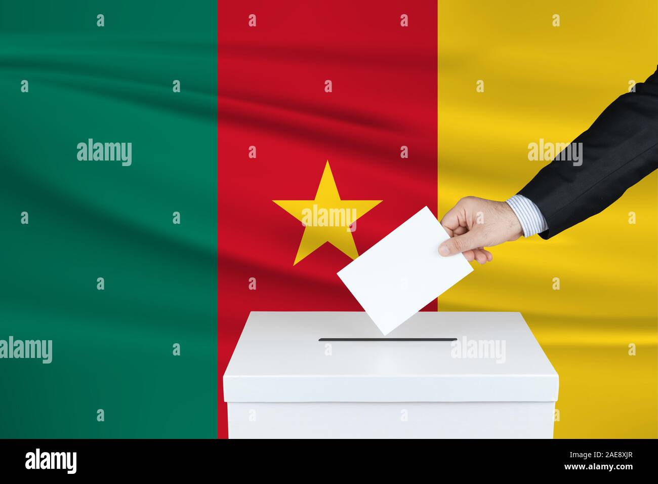 Election in Cameroon. The hand of man putting his vote in the ballot box. Waved Cameroon flag on background. Stock Photo