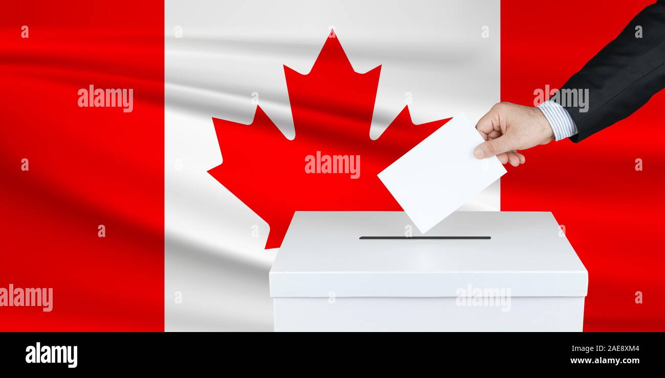 Election in Canada. The hand of man putting his vote in the ballot box. Waved Canada flag on background. Stock Photo