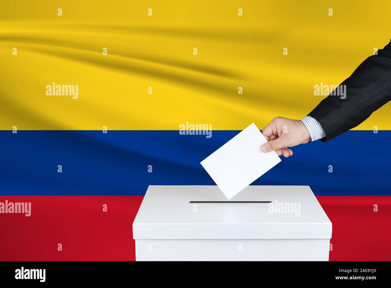 Election in Columbia. The hand of man putting his vote in the ballot box. Waved Columbia flag on background. Stock Photo