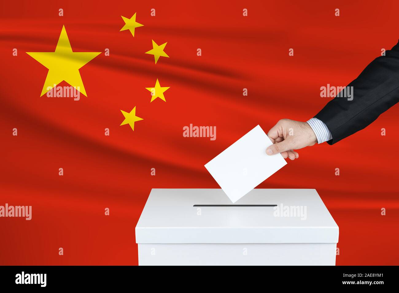 Election in China. The hand of man putting his vote in the ballot box. Waved China flag on background. Stock Photo