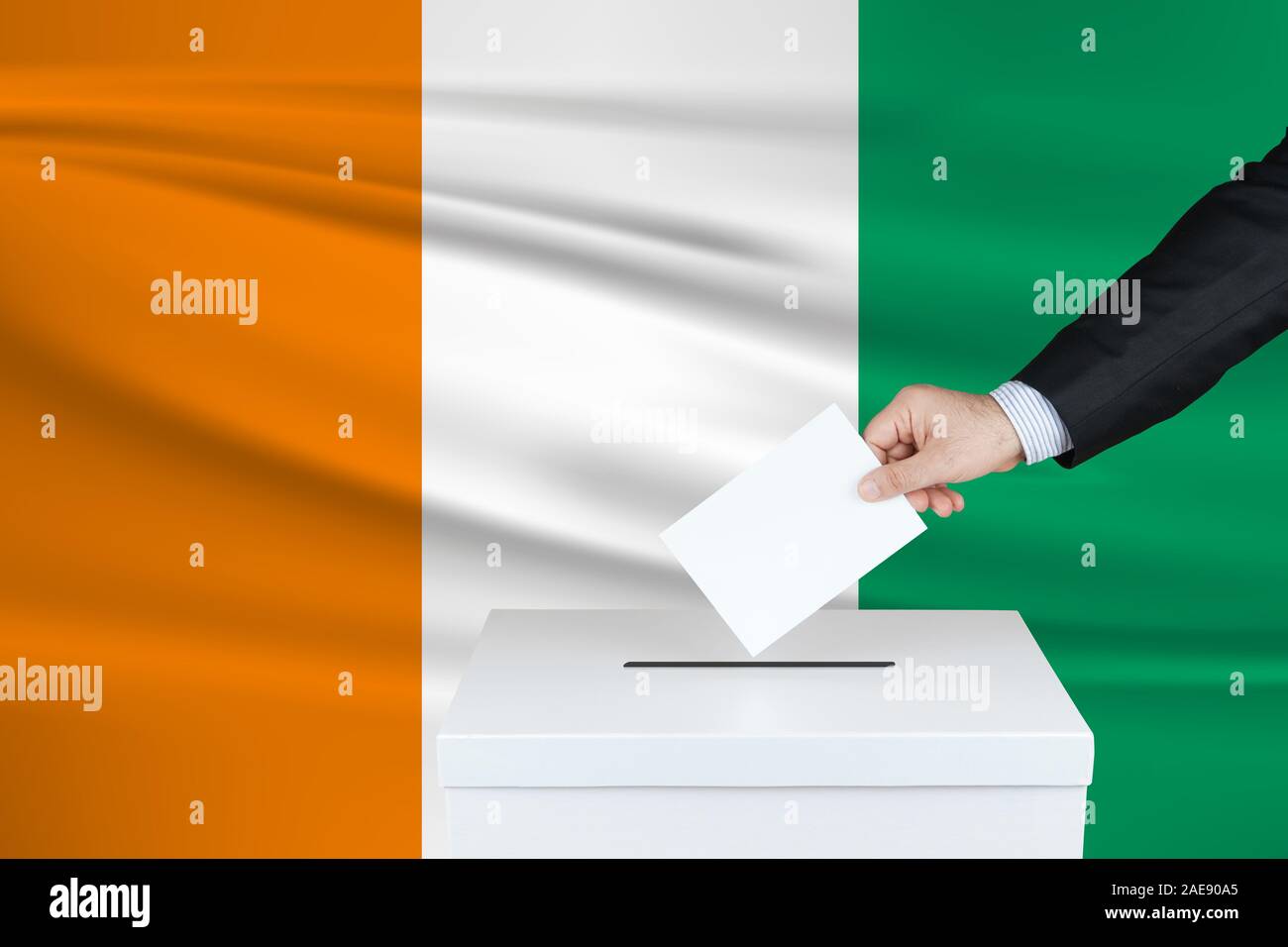 Election in Ireland. The hand of man putting his vote in the ballot box. Waved Ireland flag on background. Stock Photo