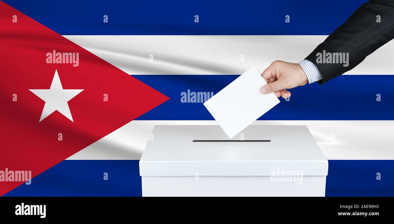 Election in Cuba. The hand of man putting his vote in the ballot box. Waved Cuba flag on background. Stock Photo