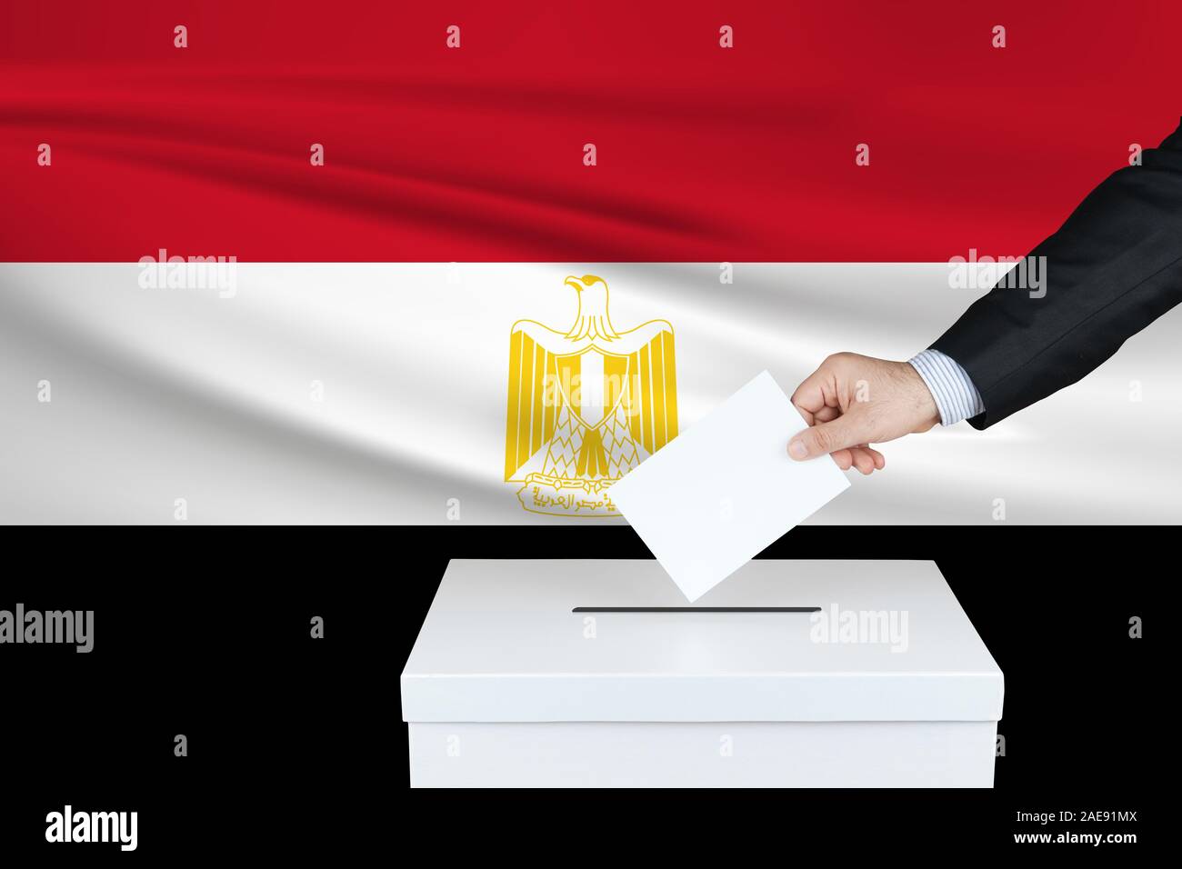 Election in Egypt. The hand of man putting his vote in the ballot box. Waved Egypt flag on background. Stock Photo