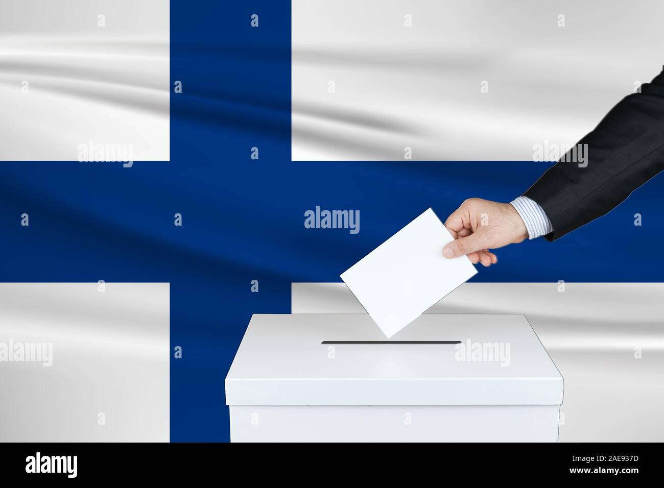 Election in Finland. The hand of man putting his vote in the ballot box. Waved Finland flag on background. Stock Photo