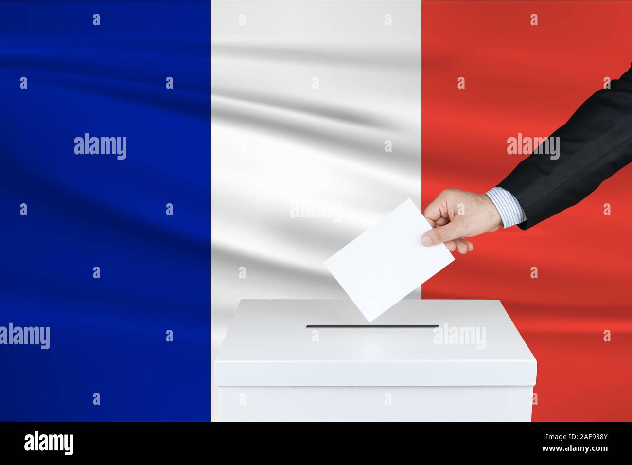 Election in France. The hand of man putting his vote in the ballot box. Waved France flag on background. Stock Photo