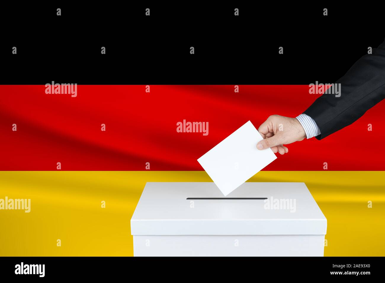Election in Germany. The hand of man putting his vote in the ballot box. Waved Germany flag on background. Stock Photo