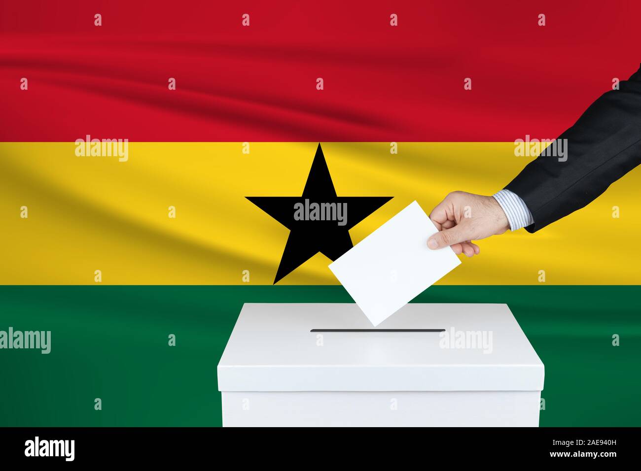 Election in Ghana. The hand of man putting his vote in the ballot box. Waved Ghana flag on background. Stock Photo