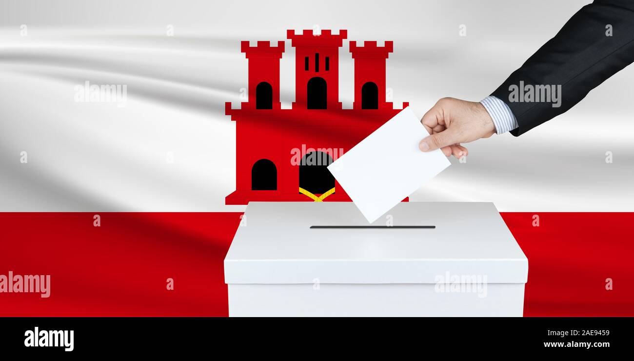 Election in Gilibrator. The hand of man putting his vote in the ballot box. Waved Gilbrator flag on background. Stock Photo
