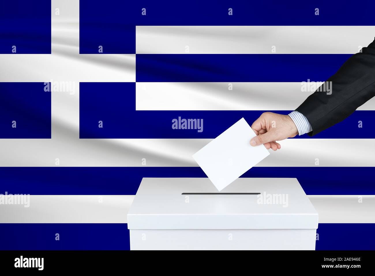 Election in Greece. The hand of man putting his vote in the ballot box. Waved Greece flag on background. Stock Photo