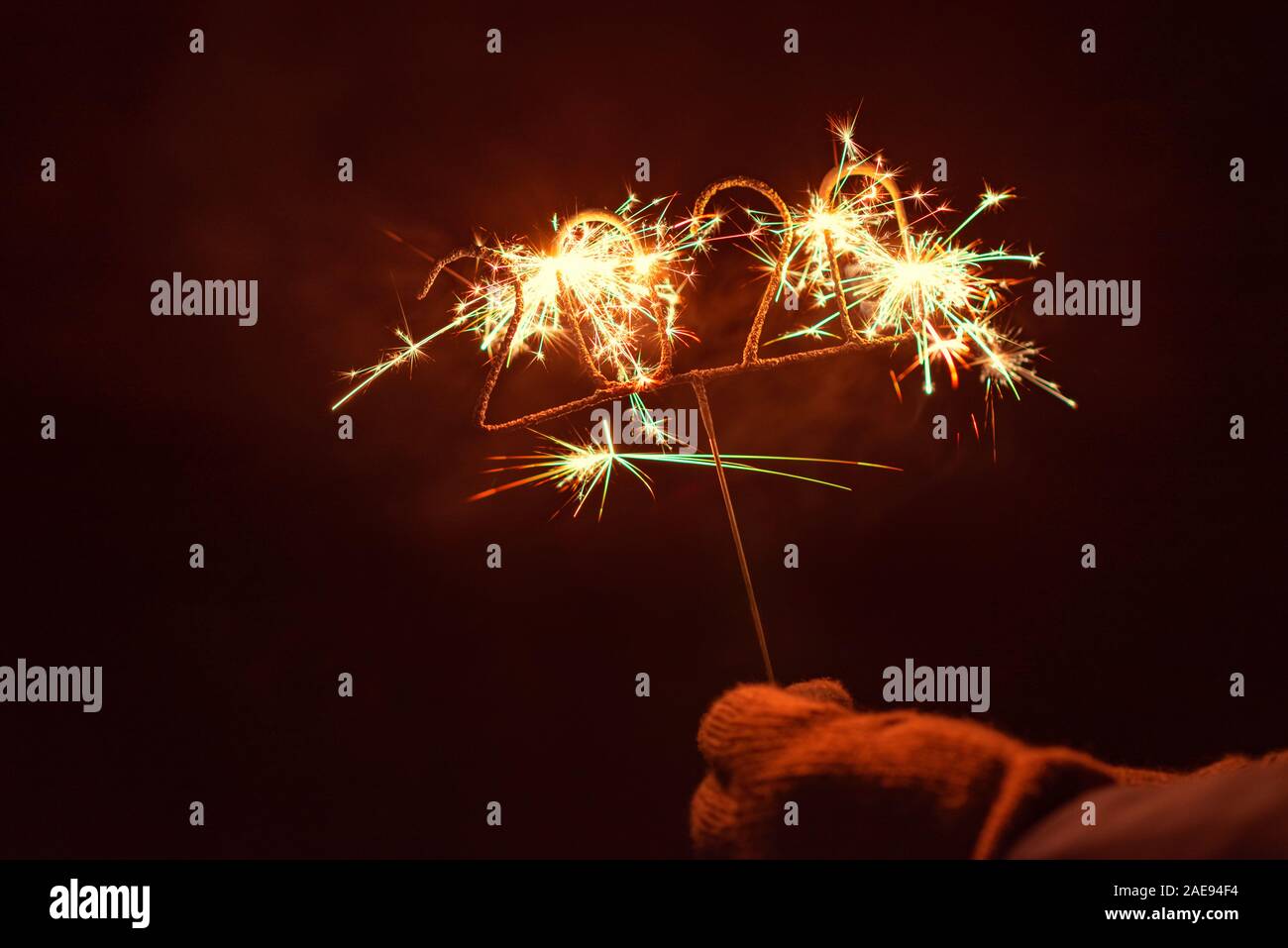 Human hand with glove holding an igniting 2020 Shaped Sparkler, outdoors at night Stock Photo