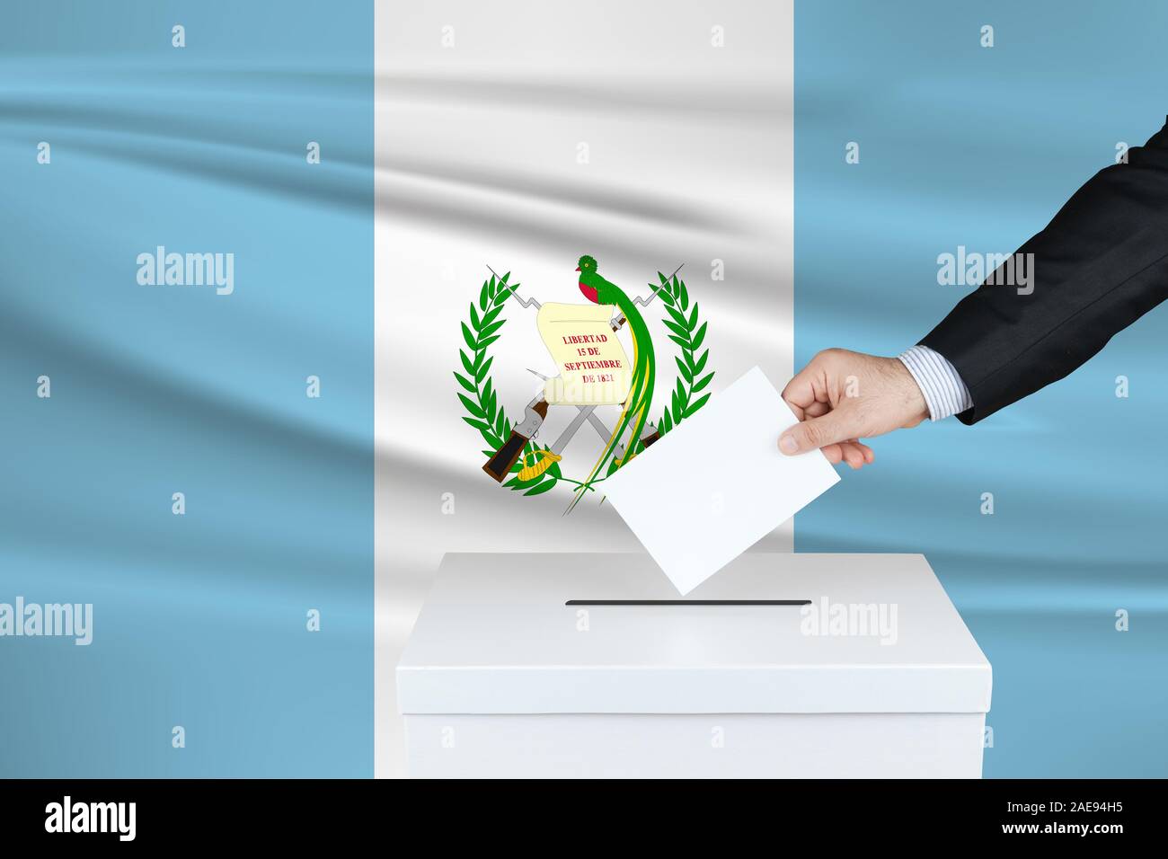 Election in Guatemala. The hand of man putting his vote in the ballot box. Waved Guatemala flag on background. Stock Photo