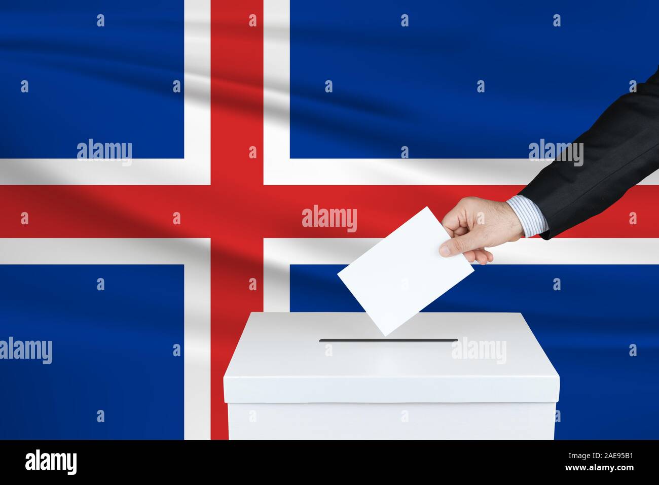 Election in Iceland. The hand of man putting his vote in the ballot box. Waved Iceland flag on background. Stock Photo