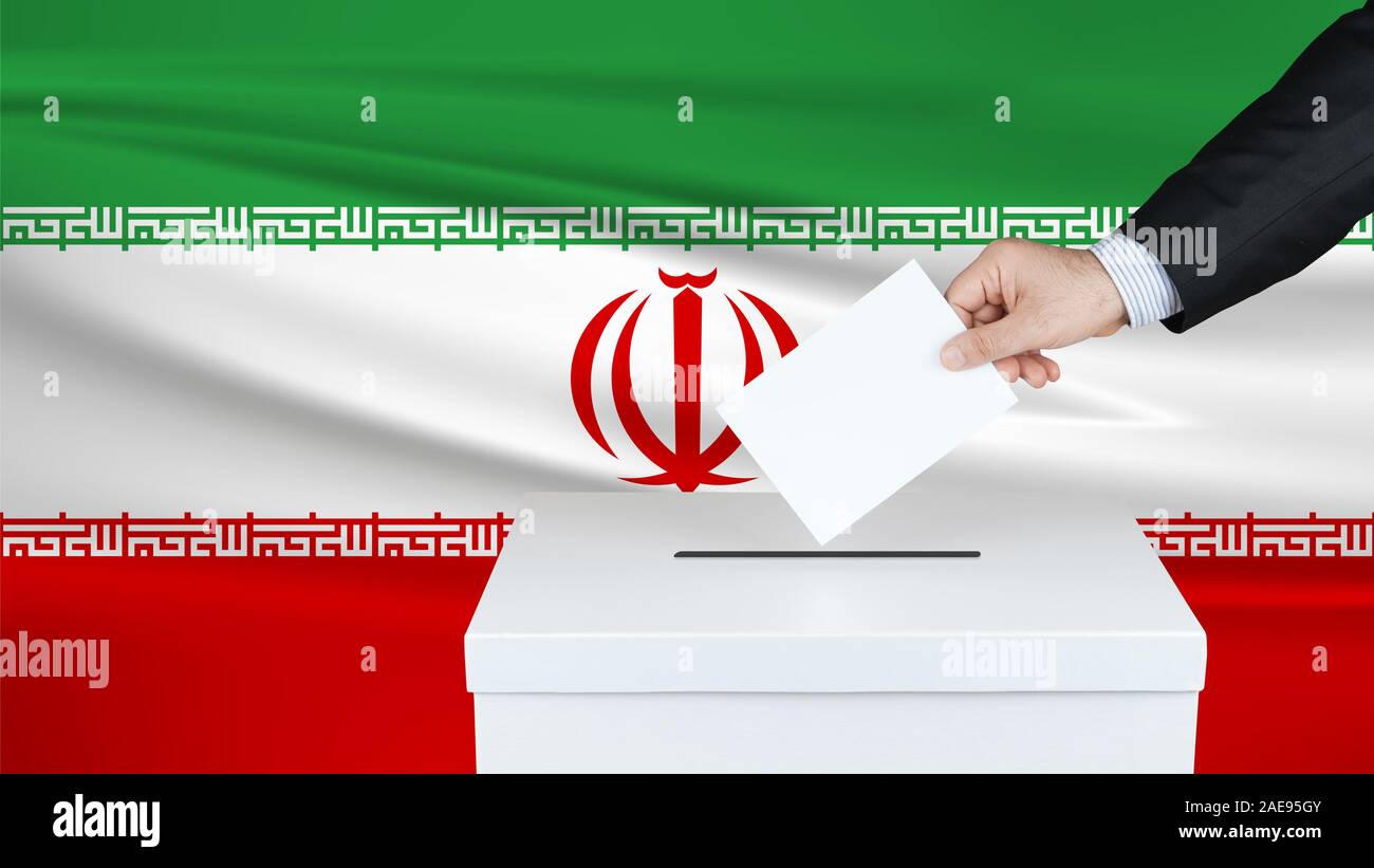 Election in Iran. The hand of man putting his vote in the ballot box. Waved Iran flag on background. Stock Photo