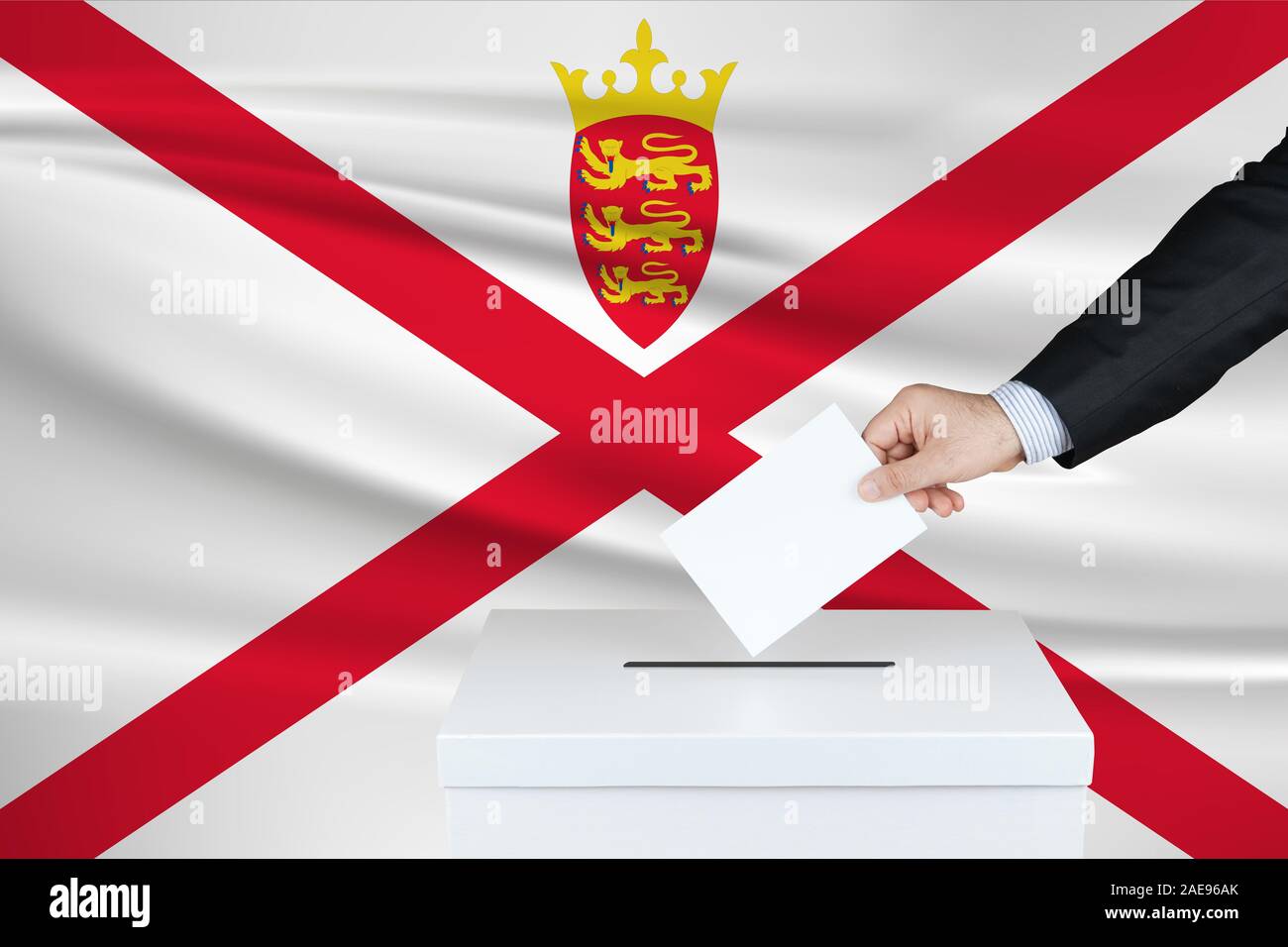 Election in Jersey. The hand of man putting his vote in the ballot box. Waved Jersey flag on background. Stock Photo
