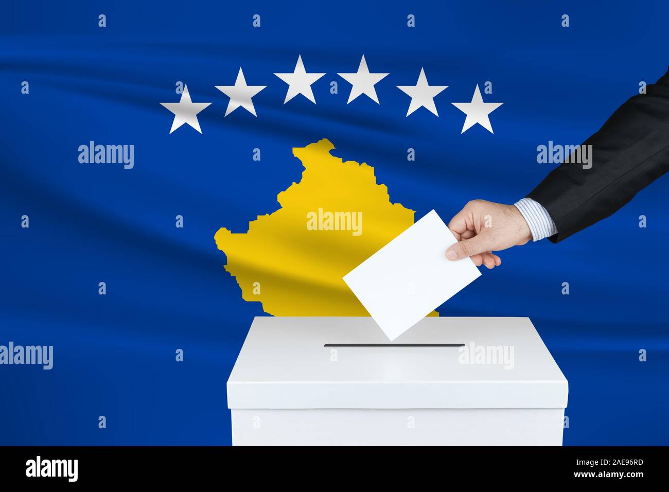 Election in Kosovo. The hand of man putting his vote in the ballot box. Waved Kosovo flag on background. Stock Photo