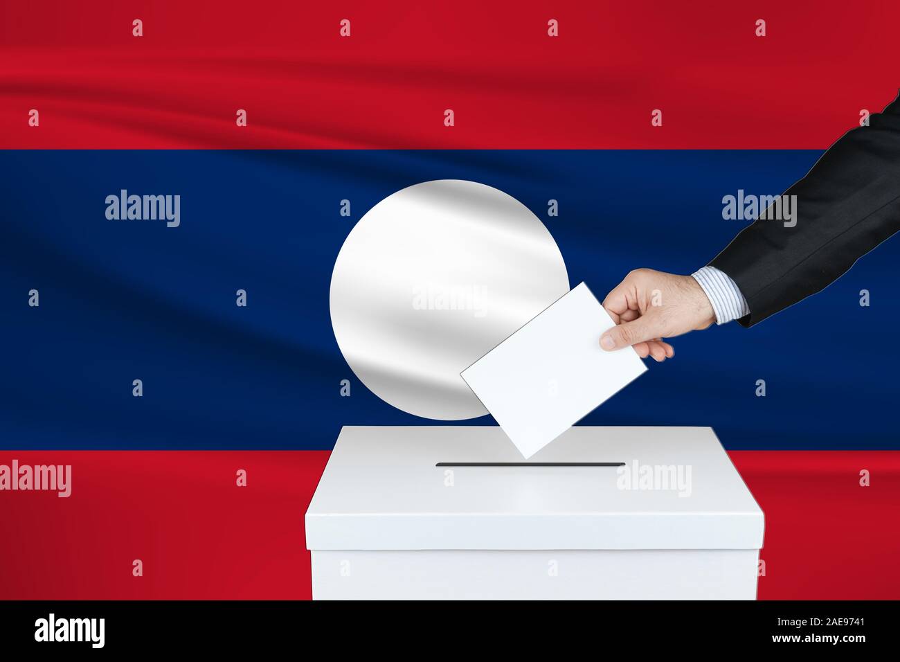 Election in Laos. The hand of man putting his vote in the ballot box. Waved Laos flag on background. Stock Photo