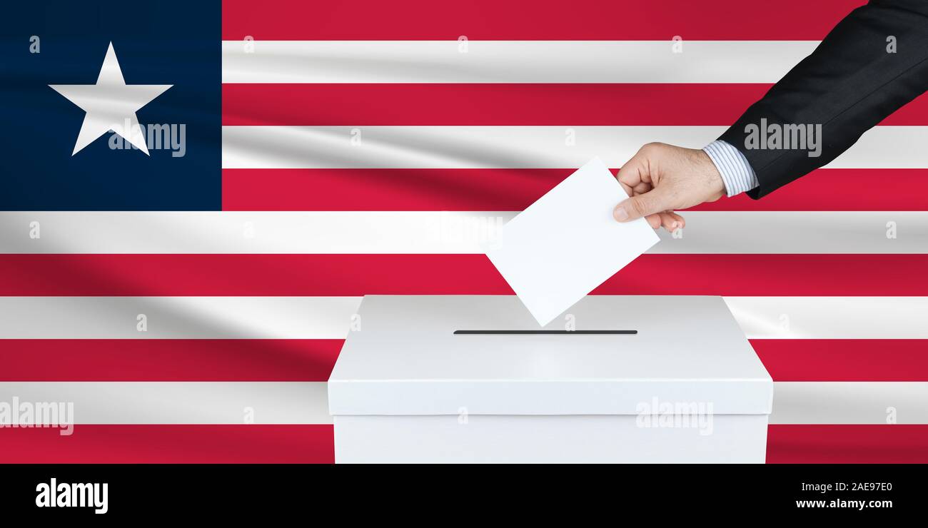 Election in Liberia. The hand of man putting his vote in the ballot box. Waved Liberia flag on background. Stock Photo