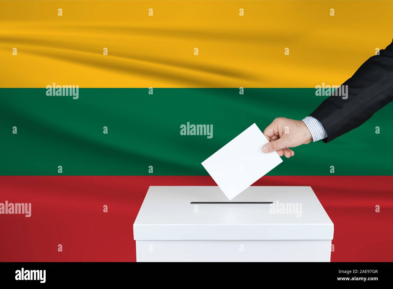 Election in Lithuania. The hand of man putting his vote in the ballot box. Waved Lithuania flag on background. Stock Photo