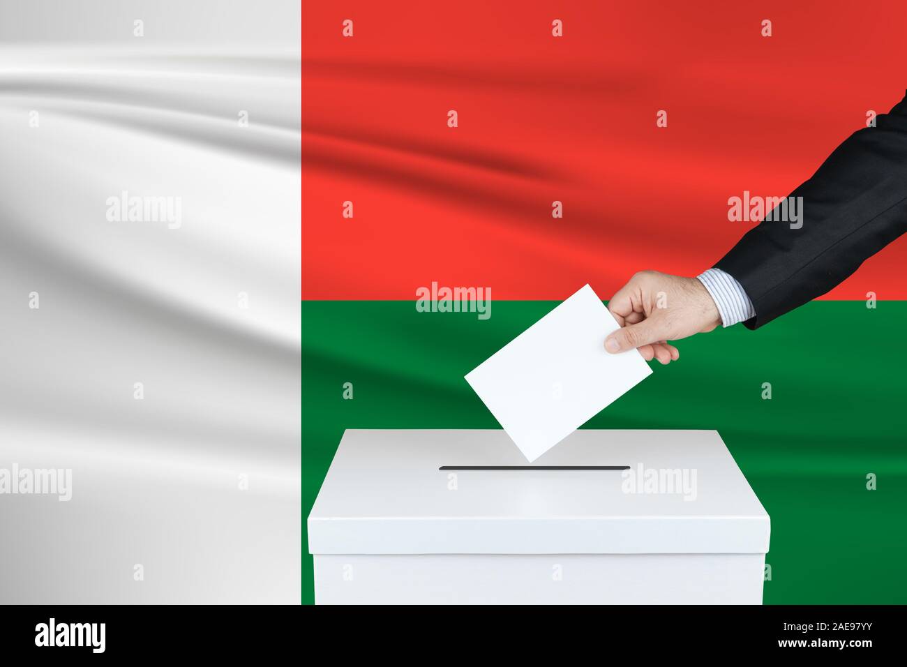 Election in Madagascar. The hand of man putting his vote in the ballot box. Waved Madagascar flag on background. Stock Photo