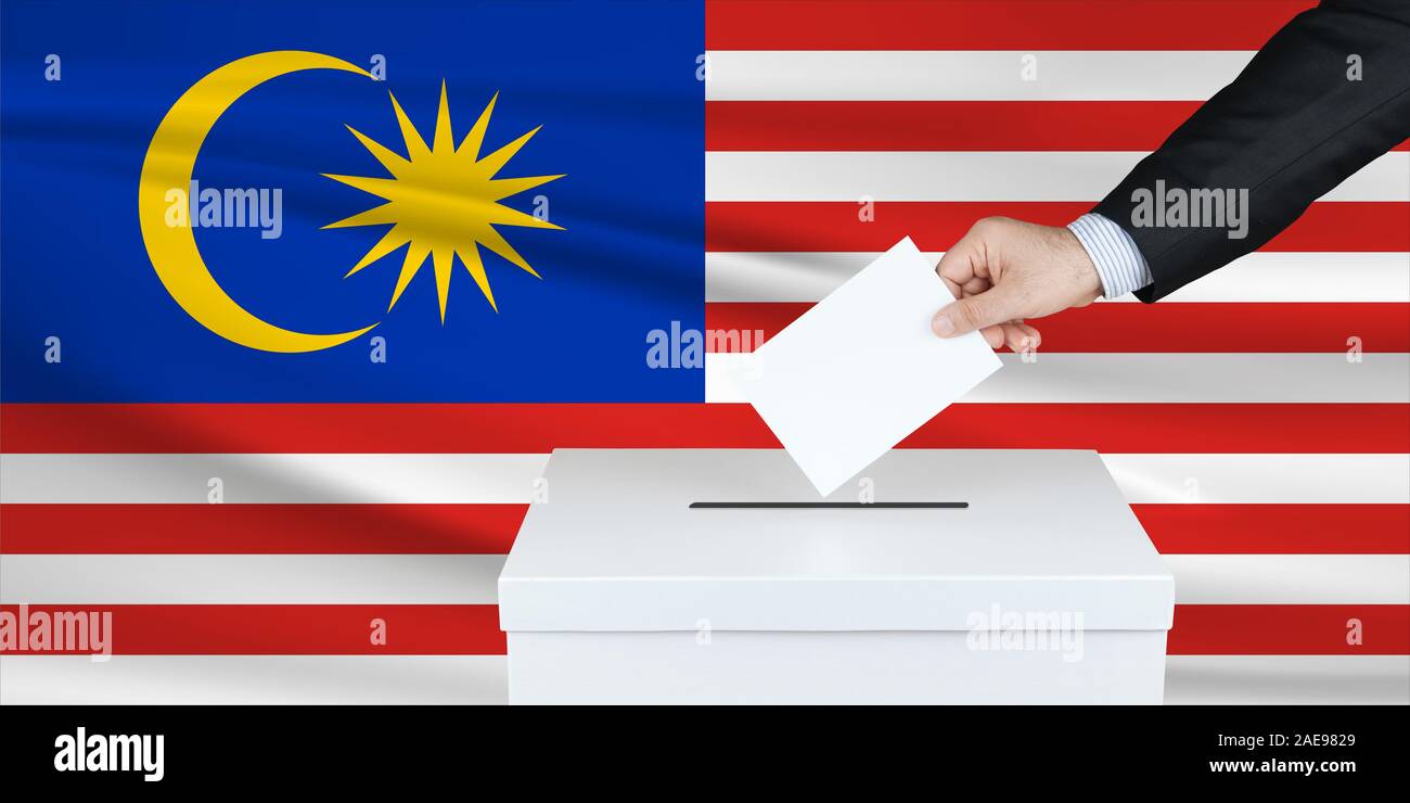 Election in Malaysia. The hand of man putting his vote in the ballot box. Waved Malaysia flag on background. Stock Photo