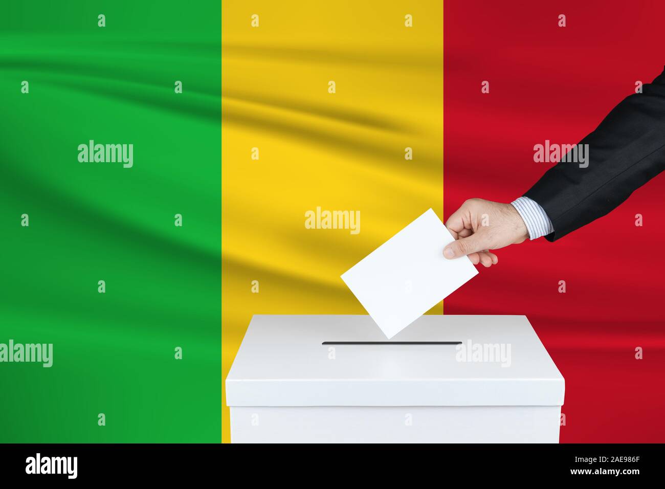 Election in Mali. The hand of man putting his vote in the ballot box. Waved Mali flag on background. Stock Photo