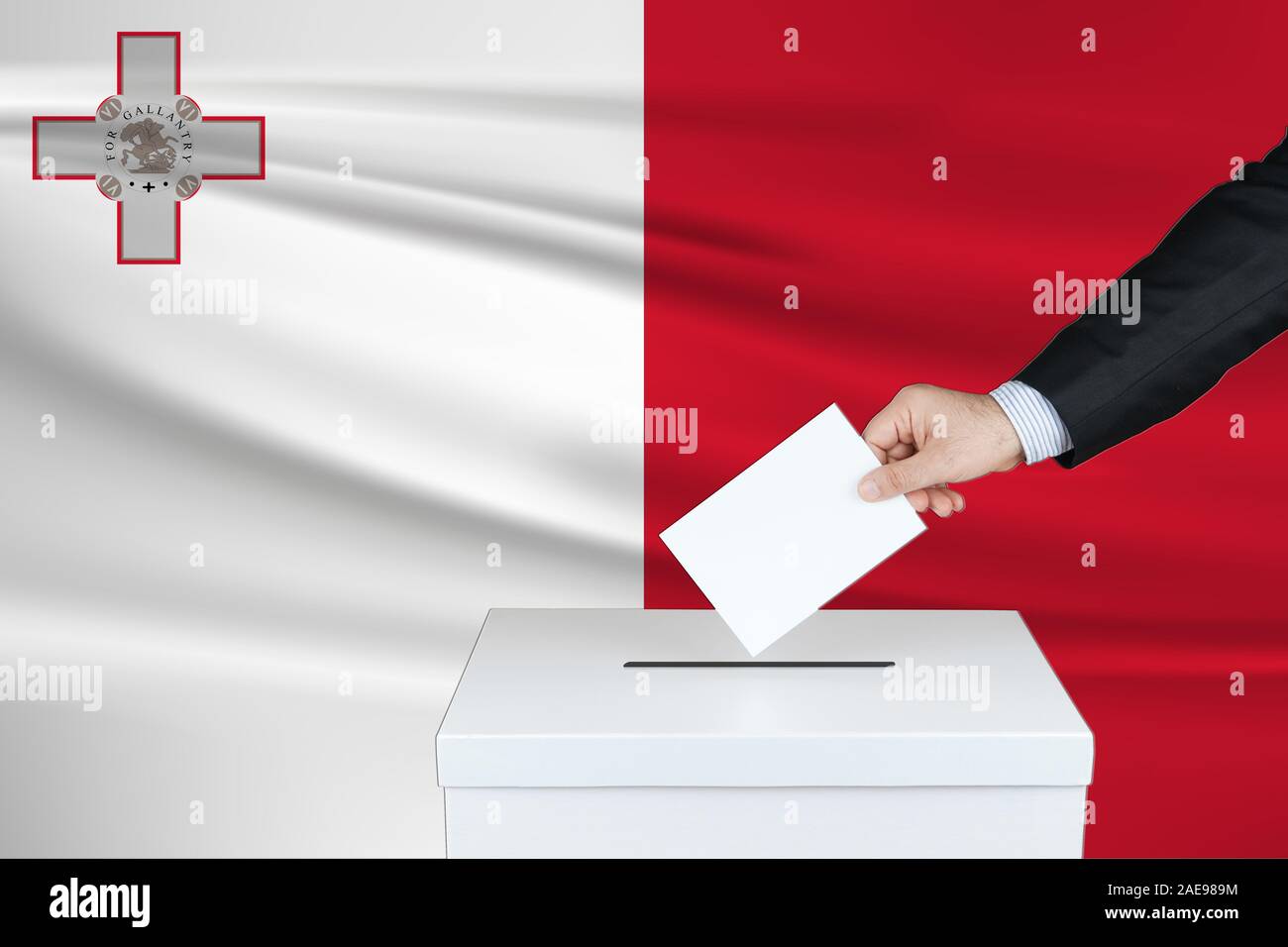 Election in Malta. The hand of man putting his vote in the ballot box. Waved Malta flag on background. Stock Photo