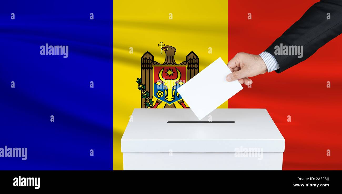 Election in Moldova. The hand of man putting his vote in the ballot box. Waved Moldova flag on background. Stock Photo