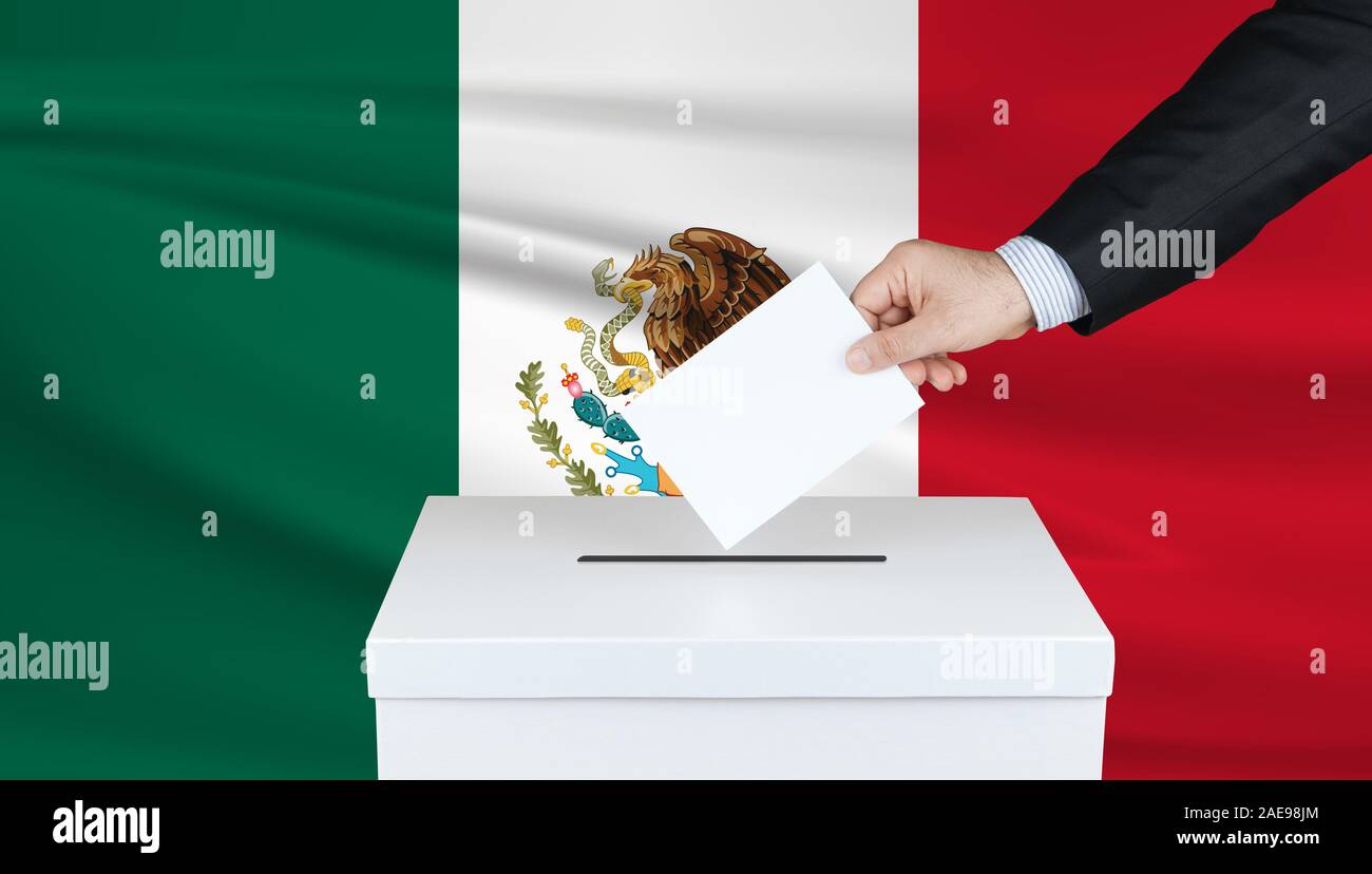 Election in Mexico. The hand of man putting his vote in the ballot box. Waved Mexico flag on background. Stock Photo