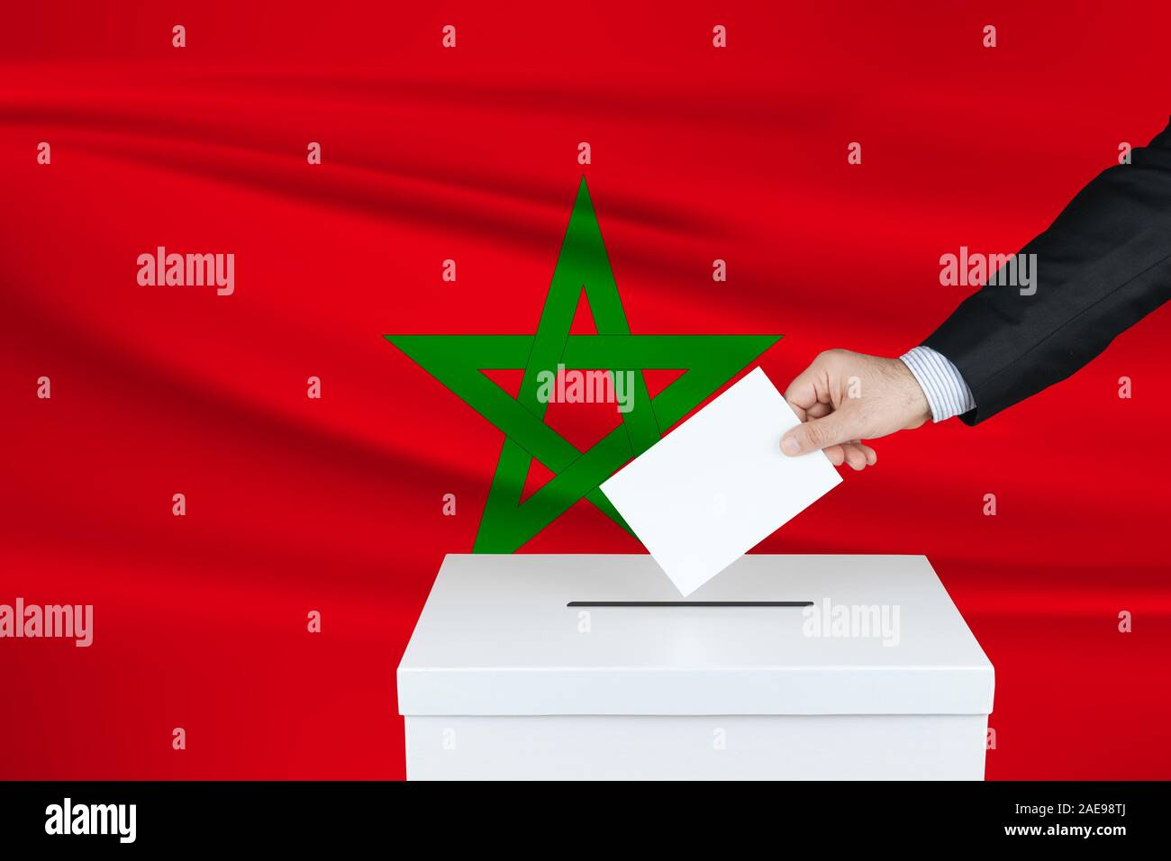 Election in Morocco. The hand of man putting his vote in the ballot box. Waved Morocco flag on background. Stock Photo
