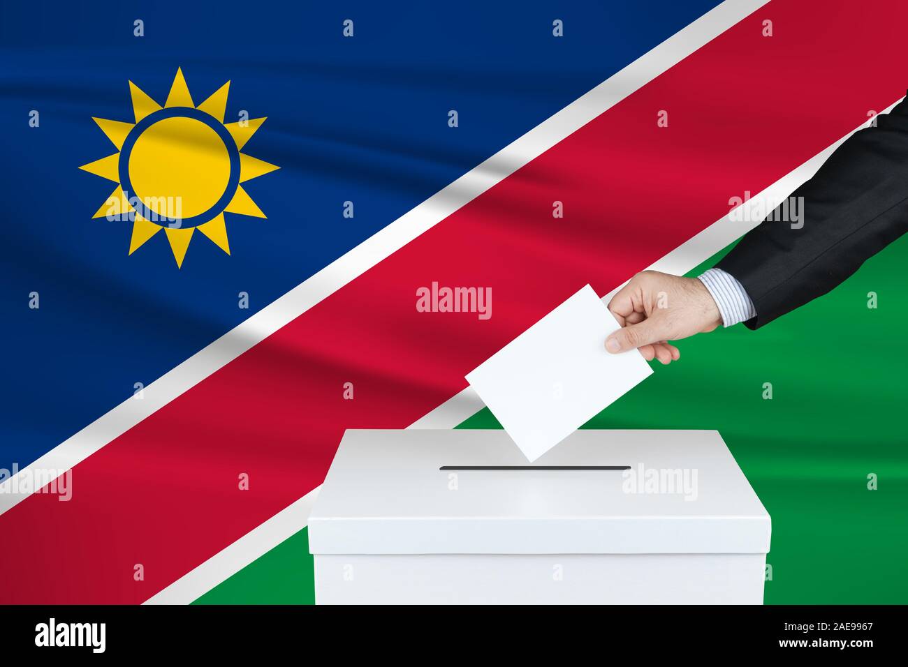 Election in Namibia. The hand of man putting his vote in the ballot box. Waved Namibia flag on background. Stock Photo