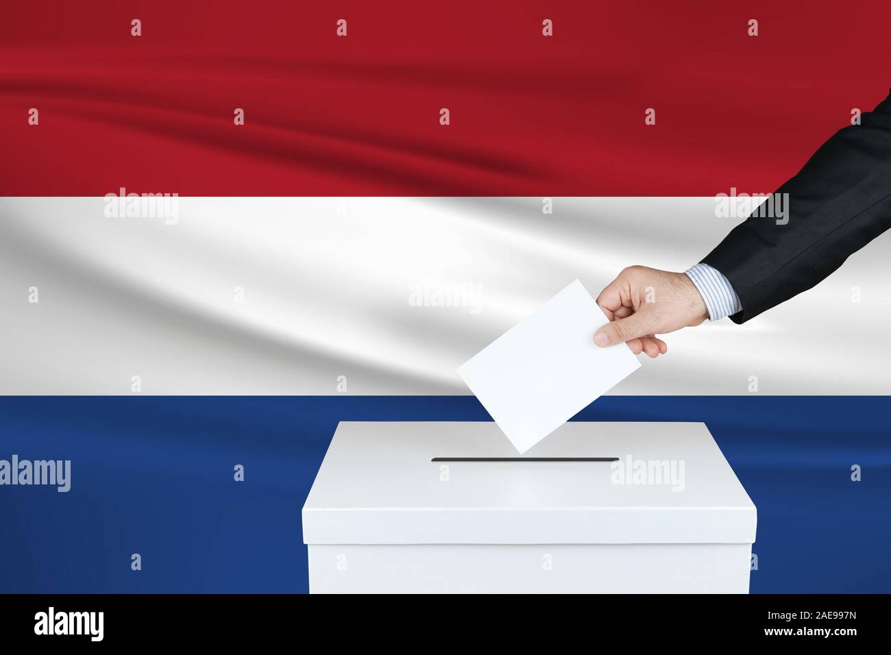 Election in Netherlands. The hand of man putting his vote in the ballot box. Waved Netherlands flag on background. Stock Photo