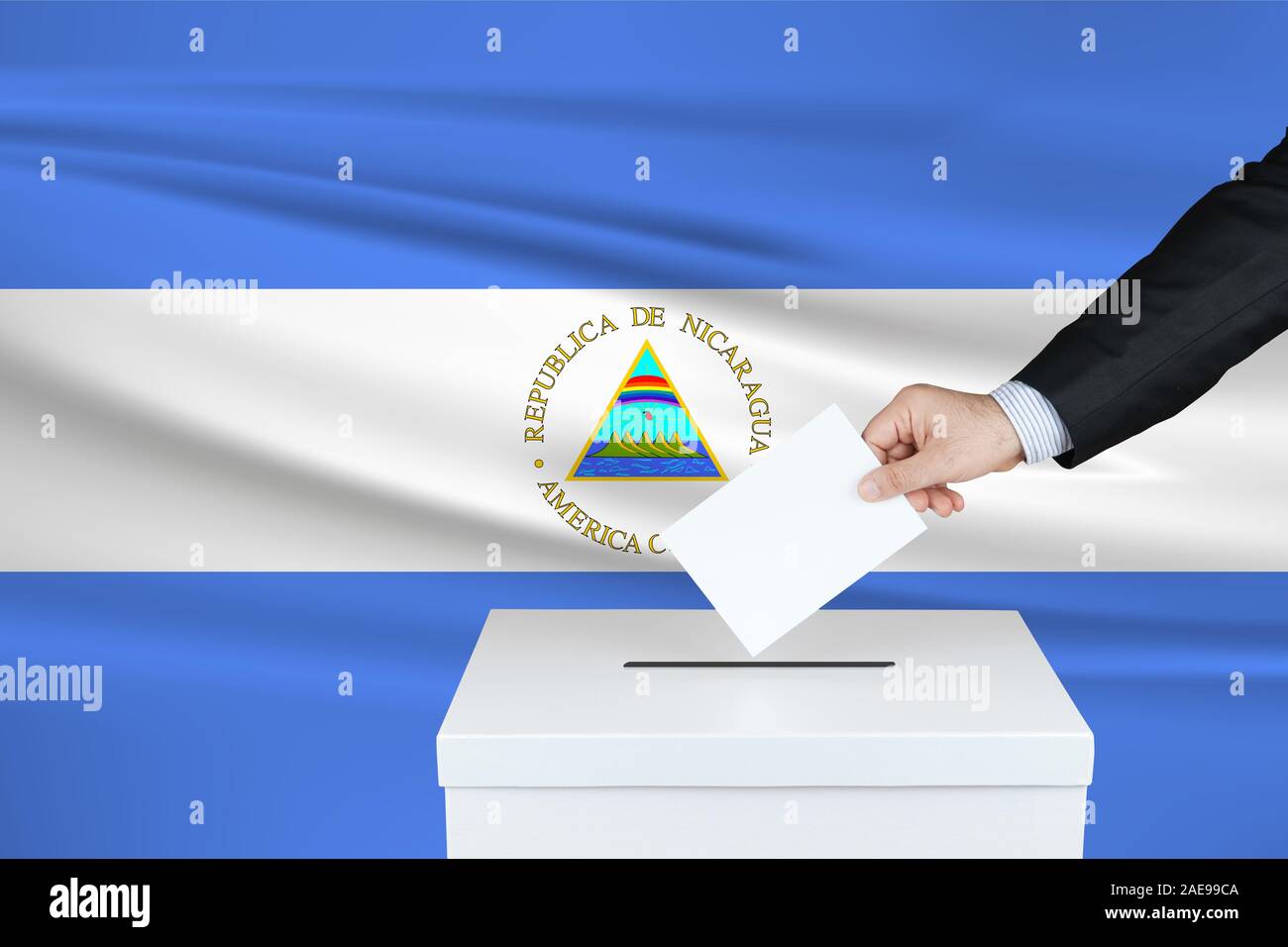 Election in Nicaragua. The hand of man putting his vote in the ballot box. Waved Nicaragua flag on background. Stock Photo