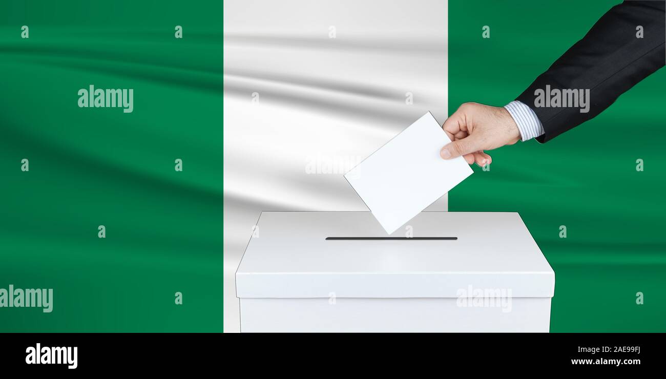Election in Nigeria. The hand of man putting his vote in the ballot box. Waved Nigeria flag on background. Stock Photo