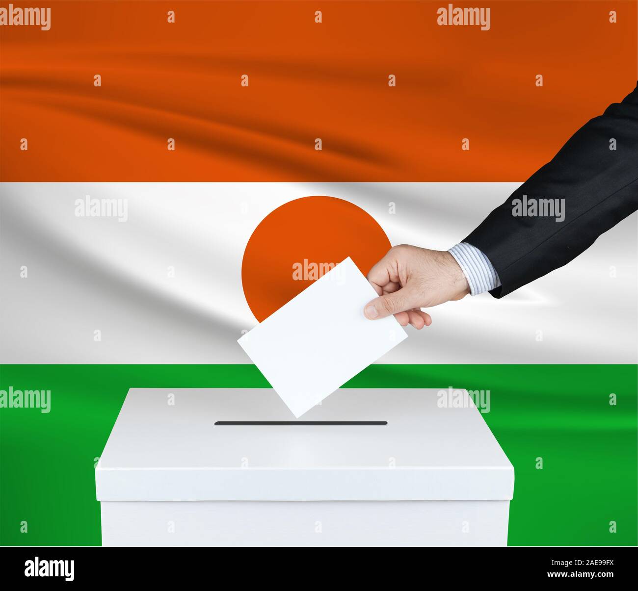 Election in Niger. The hand of man putting his vote in the ballot box. Waved Niger flag on background. Stock Photo