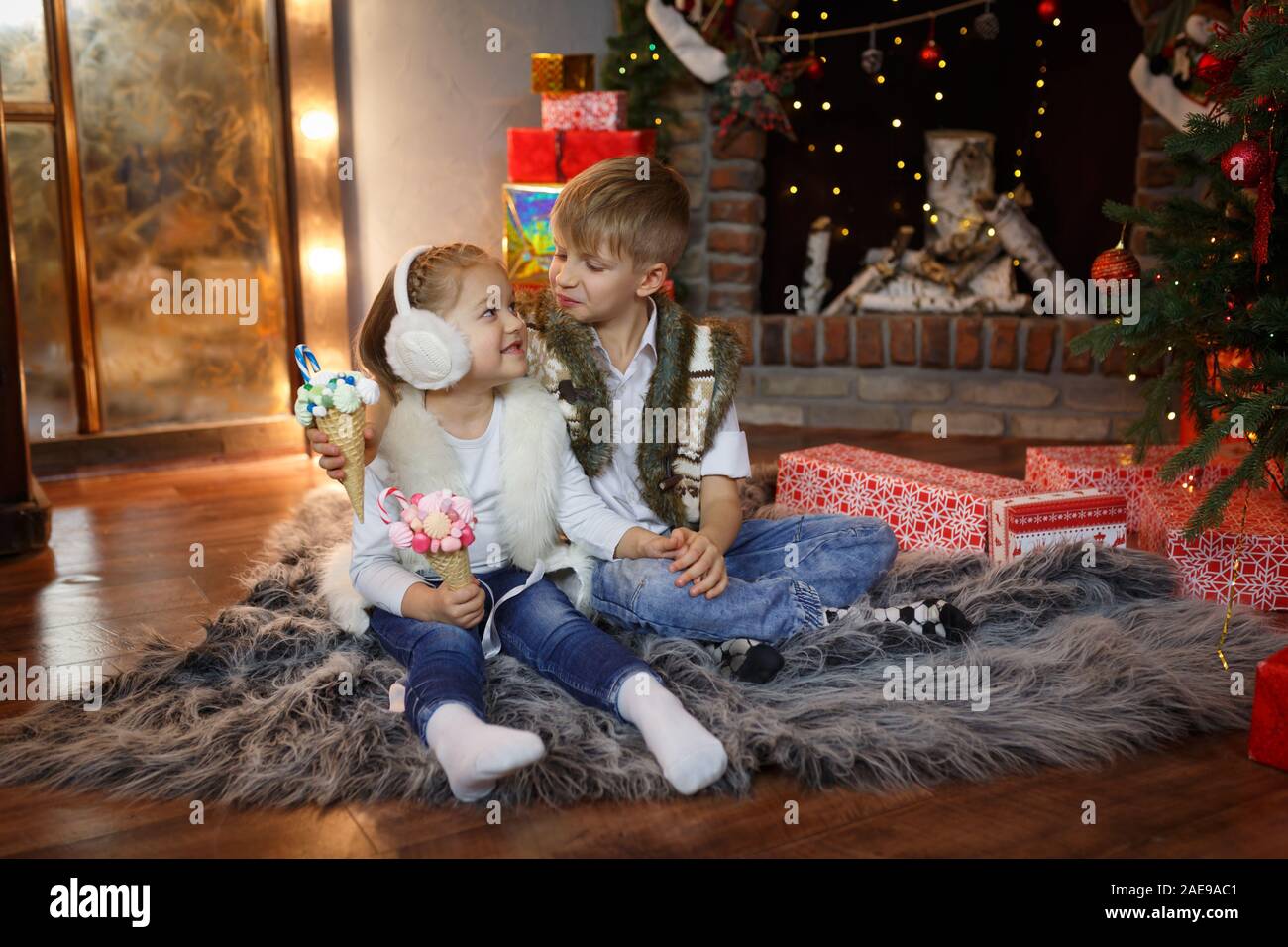 Happy children sit on the floor near the New Year tree and eat their sweet gifts Stock Photo