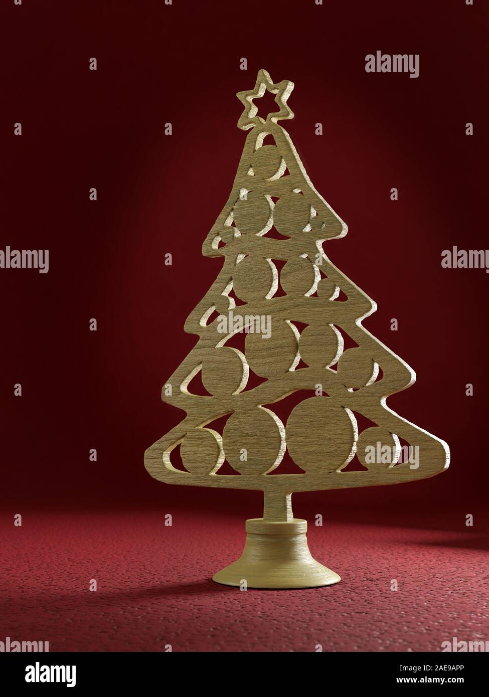 Wooden ornamental cut-out christmas tree on stand on dark red background Stock Photo