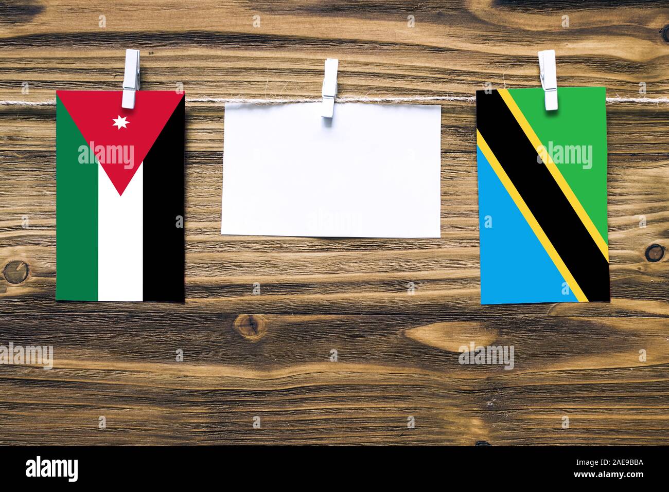 Hanging flags of Jordan and Tanzania attached to rope with clothes pins with copy space on white note paper on wooden background.Diplomatic relations Stock Photo
