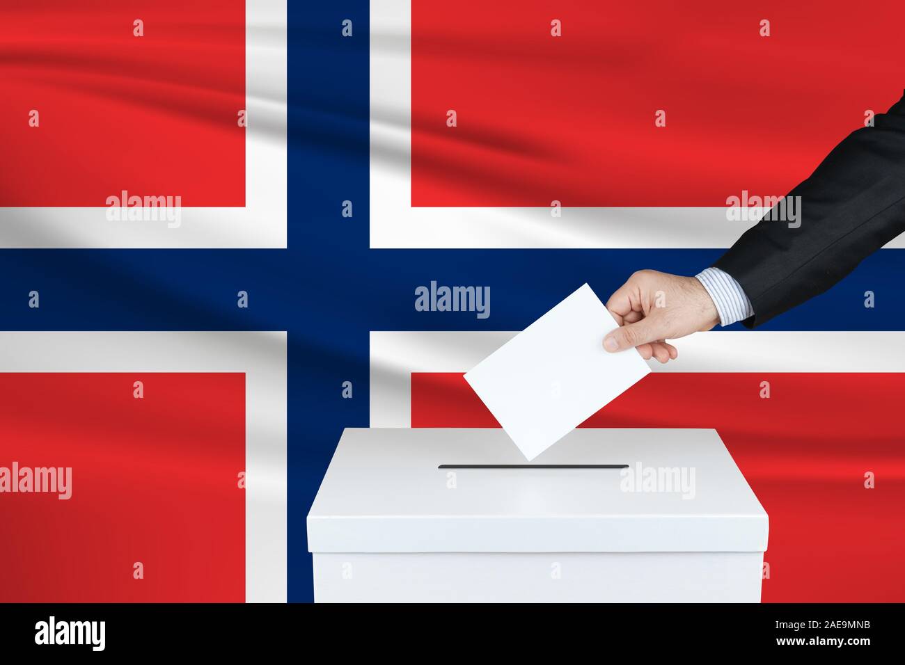 Election in Norway. The hand of man putting his vote in the ballot box. Waved Norway flag on background. Stock Photo