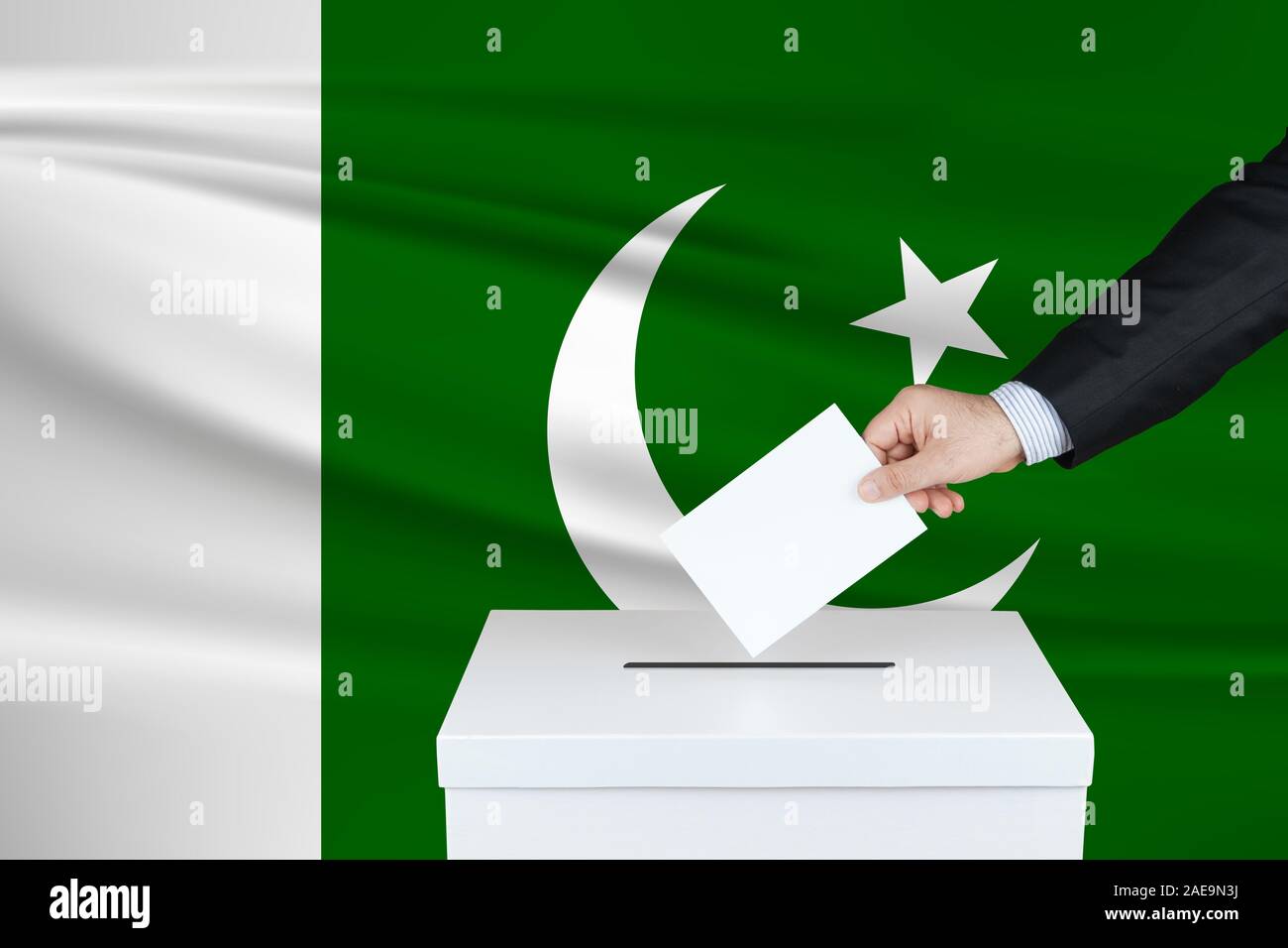 Election in Pakistan. The hand of man putting his vote in the ballot box. Waved Pakistan flag on background. Stock Photo