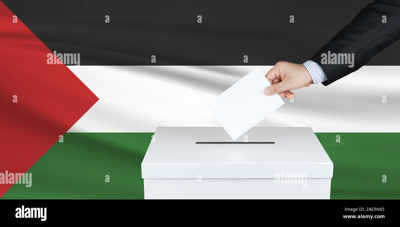 Election in Palestine. The hand of man putting his vote in the ballot box. Waved Palestine flag on background. Stock Photo