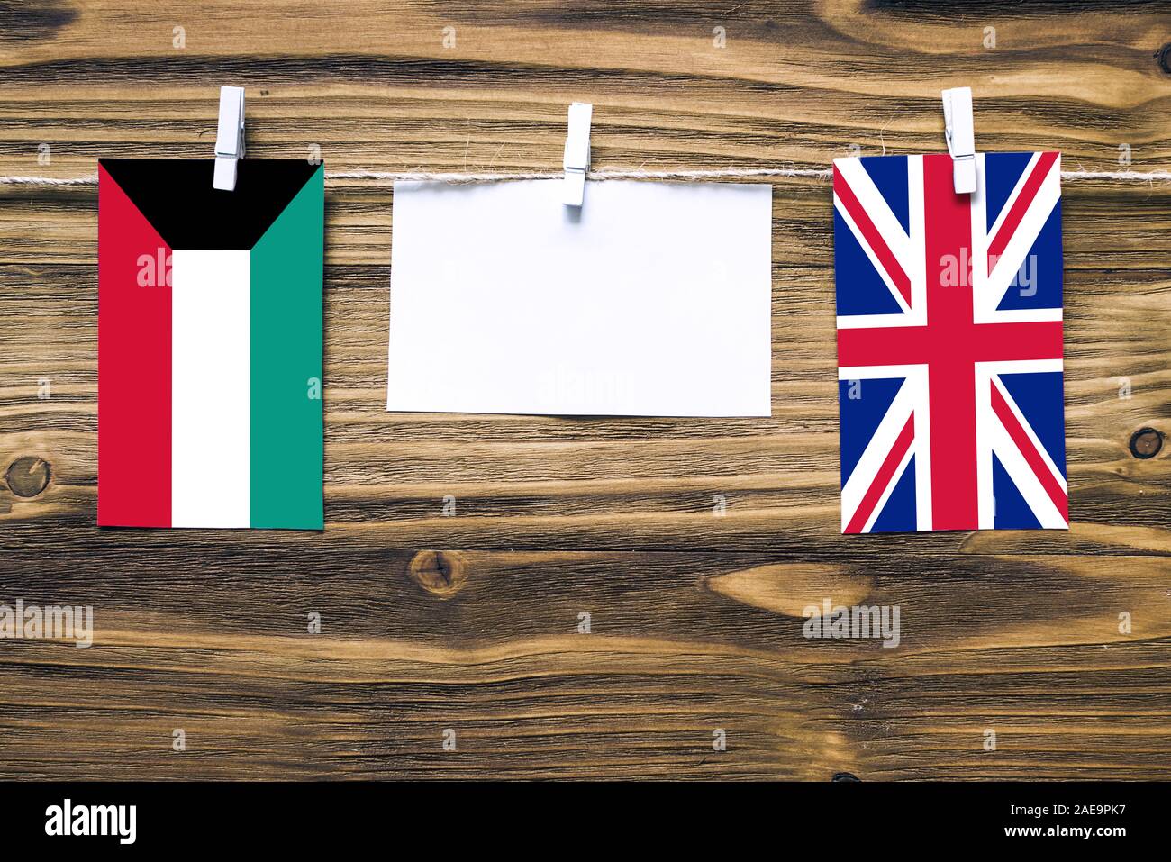 Hanging flags of Kuwait and United Kingdom attached to rope with clothes pins with copy space on white note paper on wooden background.Diplomatic rela Stock Photo