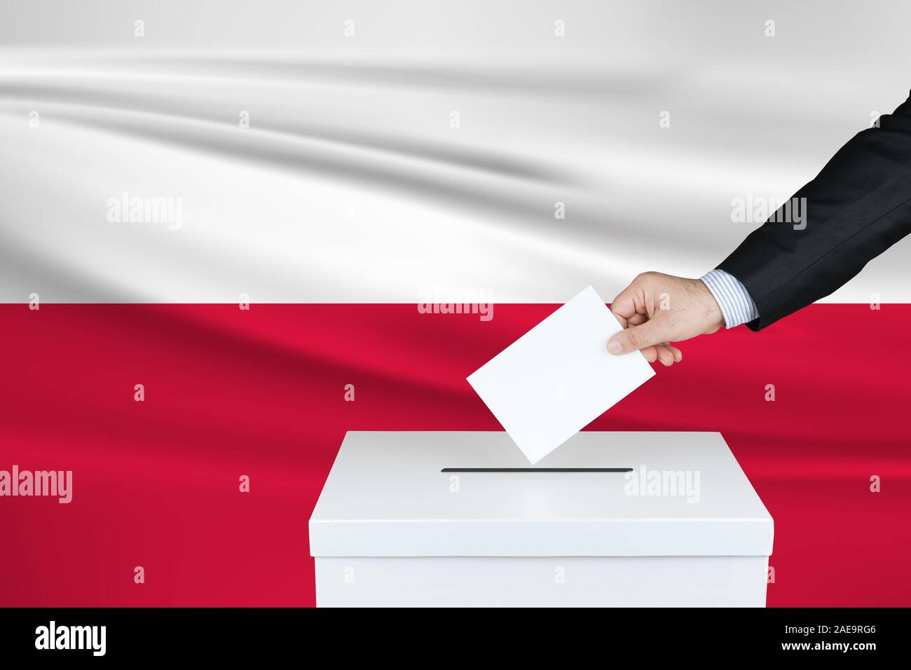 Election in Poland. The hand of man putting his vote in the ballot box. Waved Poland flag on background. Stock Photo
