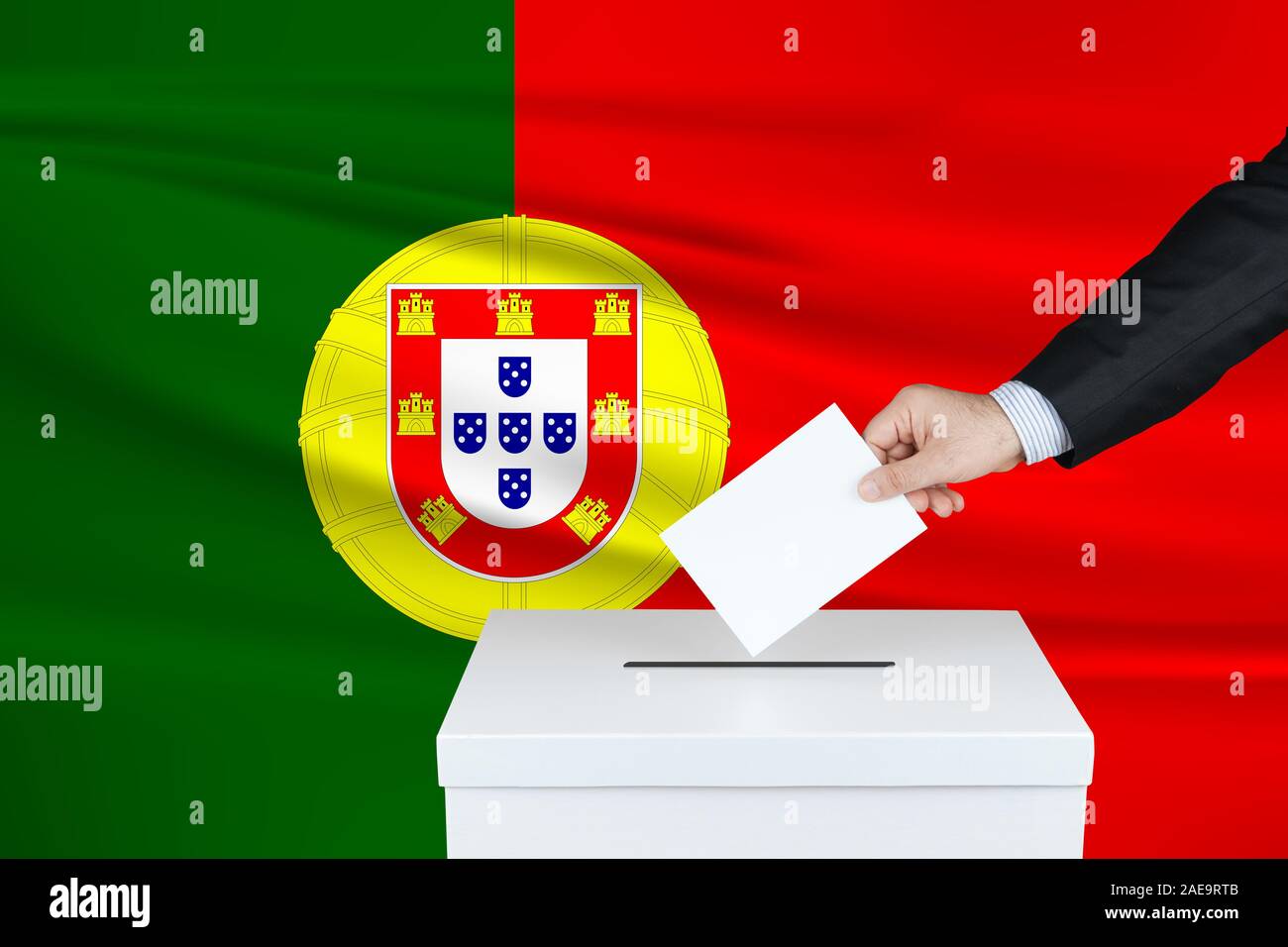 Election in Portugal. The hand of man putting his vote in the ballot box. Waved Portugal flag on background. Stock Photo