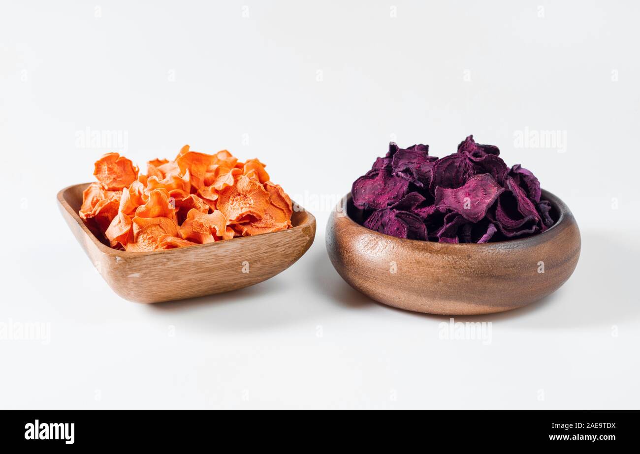 Dried carrot and beet chips in a wooden bowl on a white background. Vegetarian diet food. Horizontal orientation. Close up. Stock Photo