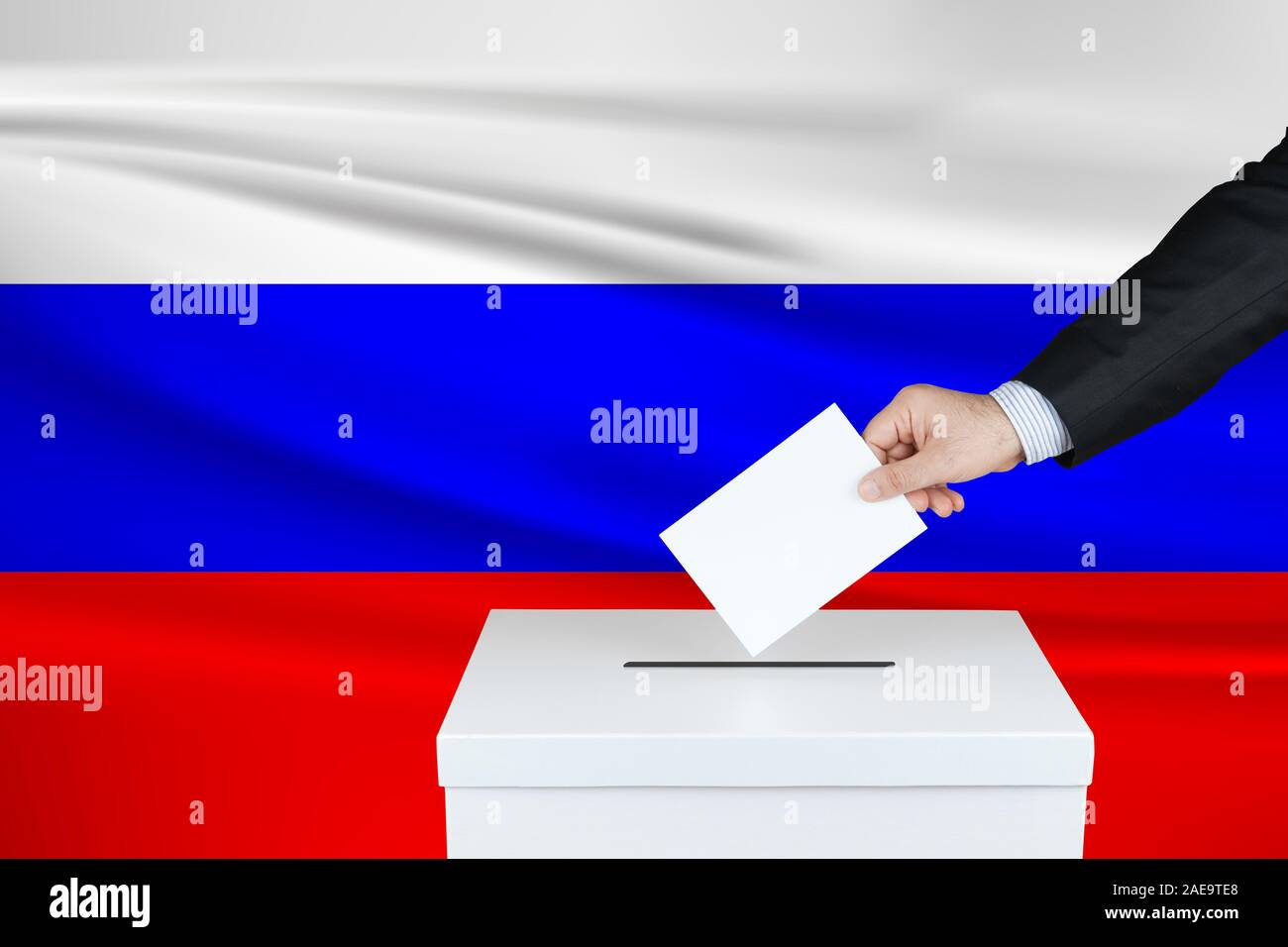 Election in Russia. The hand of man putting his vote in the ballot box. Waved Russia flag on background. Stock Photo