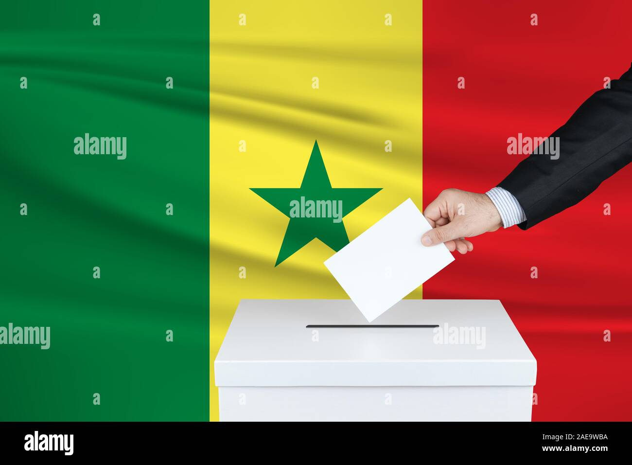 Election in Senegal. The hand of man putting his vote in the ballot box. Waved Senegal flag on background. Stock Photo