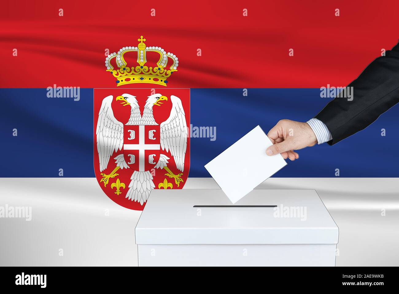 Election in Serbia. The hand of man putting his vote in the ballot box. Waved Serbia flag on background. Stock Photo