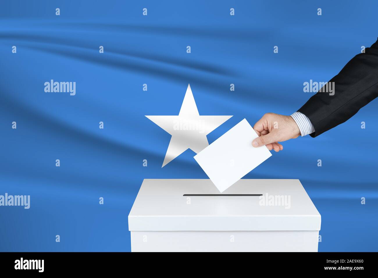 Election in Somalia. The hand of man putting his vote in the ballot box. Waved Somalia flag on background. Stock Photo